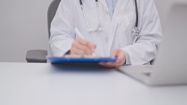 Professional doctor wearing lab coat using laptop and taking report notes on notebook for November Lung Cancer Awareness month, World Cancer Day and oncology healthcare concept in hospital