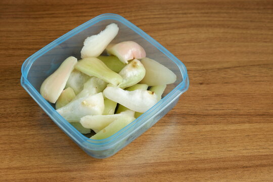 Top view of freshly cut Indonesian wax apples, known as jambu air, in a clear container on a wooden table, showcasing crisp white, green, and pink fruit pieces.