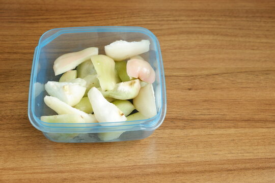 Top view of freshly cut Indonesian wax apples, known as jambu air, in a clear container on a wooden table, showcasing crisp white, green, and pink fruit pieces.
