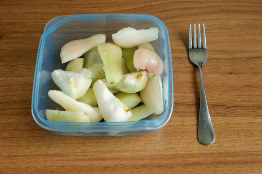Top view of freshly cut Indonesian wax apples, known as jambu air, in a clear container and a fork on a wooden table, showcasing crisp white, green, and pink fruit pieces.