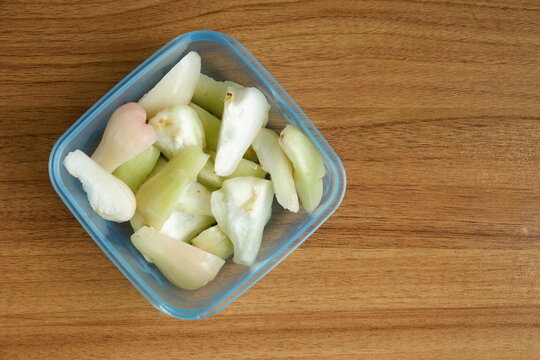 Top view of freshly cut Indonesian wax apples, known as jambu air, in a clear container on a wooden table, showcasing crisp white, green, and pink fruit pieces.
