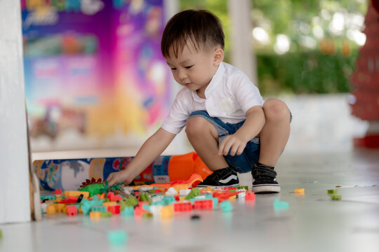 Happy Asian toddler boy playing with colorful building block toys on floor at home. Early childhood development, creative motor skill learning and preschool playtime concept.