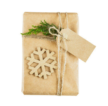 Christmas gift box wrapped in kraft paper with blank tag, wooden snowflake and green conifer branch isolated on transparent background
