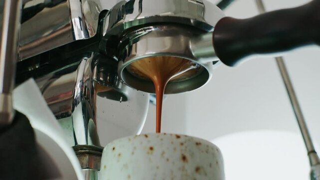 4K Pouring coffee stream from professional machine in cup. Barista man making double espresso, using filter holder. Flowing fresh ground coffee. Drinking roasted black coffee in the morning.