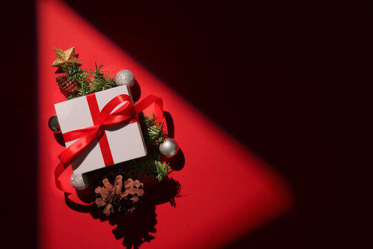 Elegant Christmas gift box with red ribbon and pine branches under spotlight
