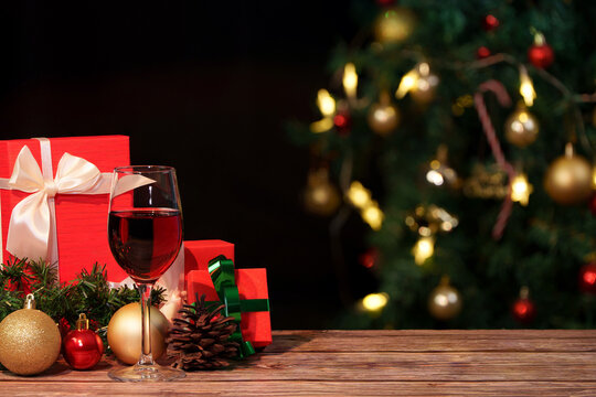 Red wine glass and Christmas gifts on wooden table with blurred tree background
