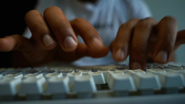 Hands typing on computer keyboard, Close-up of hands typing on a white computer keyboard in a dark workspace, showing focused work, online communication, coding, study, and technology use