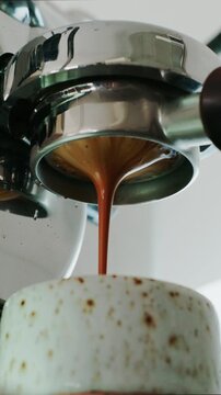 4K Pouring coffee stream from professional machine in cup. Barista man making double espresso, using filter holder. Flowing fresh ground coffee. Drinking roasted black coffee in the morning.	