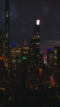 Vertical video: Sliding reveal of night city panorama. Illuminated high rise downtown buildings and wide avenues. Parallax effect. Manhattan, New York City, USA