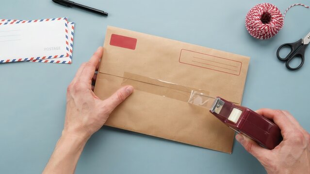 Hands sealing a brown paper envelope with tape