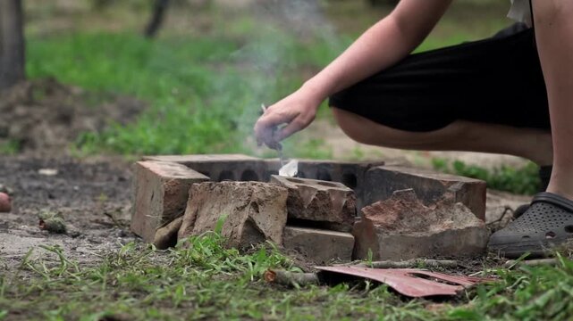 The guy throws papers into the fire to stoke the flames.