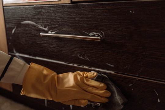 Gloved hand wiping a lower drawer with a gray cloth below a metal handle.