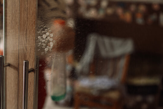 Cleaner droplets on a mirror beside a metal handle with a reflected bottle.