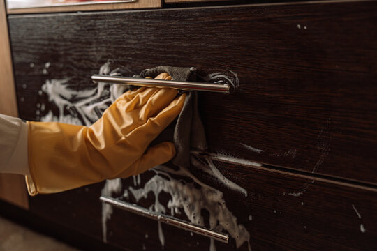Gloved hand wiping foam beneath a drawer handle with a gray cloth.