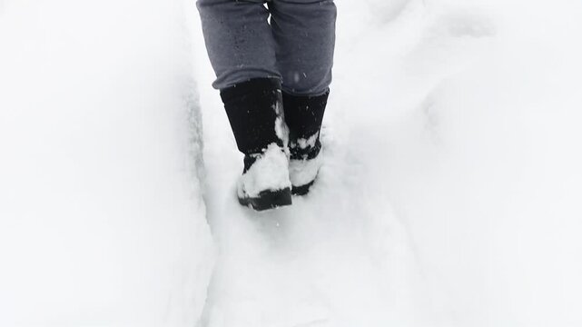 Close-up of a person walking through deep fresh snow in winter, with black boots sinking into the soft white surface. Seasonal outdoor lifestyle and cold weather concept.