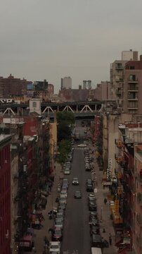 Vertical video: Low flying aerial shot of New York City Chinatown streets with car overpass and people doing their daily activities in the streets below