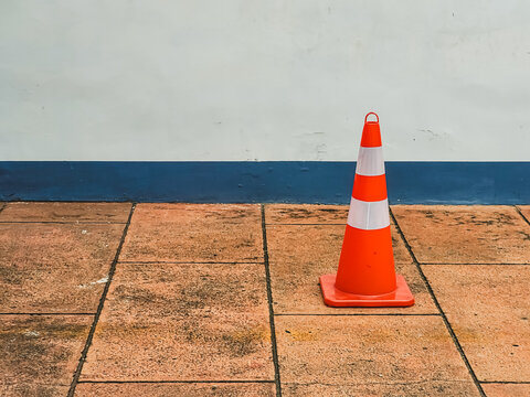 Orange traffic cone on a tiled pavement against a minimalist wall, symbolizing caution, safety, restricted access, construction work, and urban traffic management.