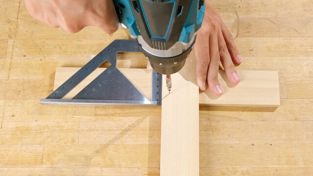 Carpenter using an electric drill and square tool on a wooden block