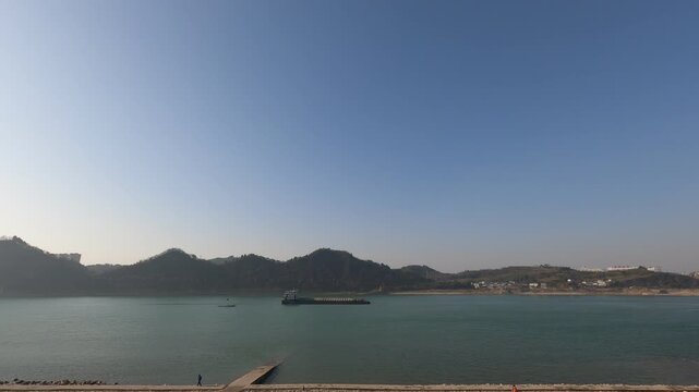 Wide calm river reservoir with cargo barge and rolling hills under clear blue sky