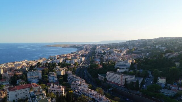 Slow aerial push over hillside homes and pine trees toward the sea, highway, railway and airport runway at golden hour, Nice, French Riviera, Cote d Azur, France