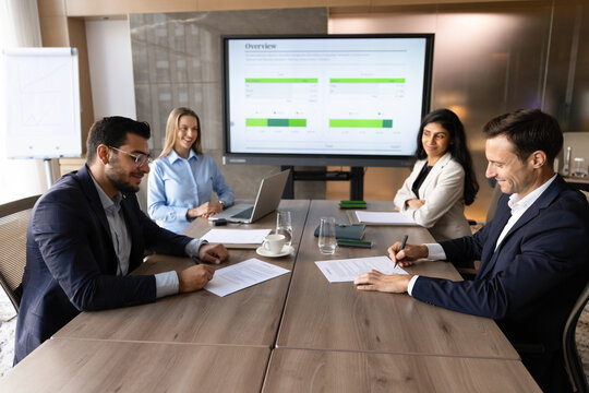 Diverse business partners sit at conference table, signing contract, completing corporate meeting, confirming legal agreement document with signature. Successful negotiation, partnership conclusion