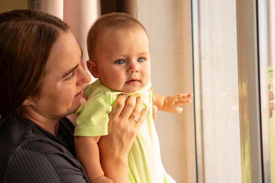 Mother Holds Baby Son Looking Through Bright Window