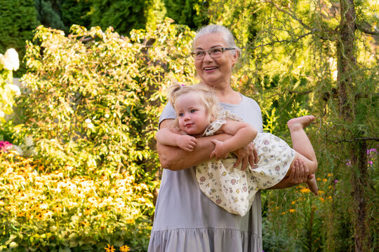 Smiling Grandmother Carrying Granddaughter in Sunny Garden