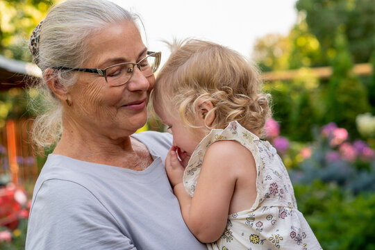 Grandmother Comforting Shy Granddaughter In Summer Garden