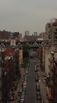 Vertical video: Low flying aerial shot of NYC Chinatown city streets with person on a rooftop and cars passing by on an overpass