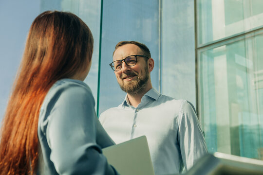 Businessman and businesswoman discussing project in office with glass doors, sunny day