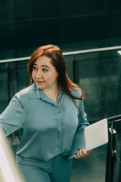 Redhead businesswoman in blue suit with laptop walking up office stairs