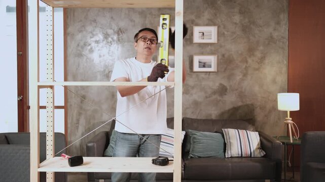 Asian mature man assembling furniture with DIY tools, checking accuracy with spirit&nbsp;level, achievement satisfied, cheerful and proud home improvement, hobby wooden workshop handyman, active lifestyle.