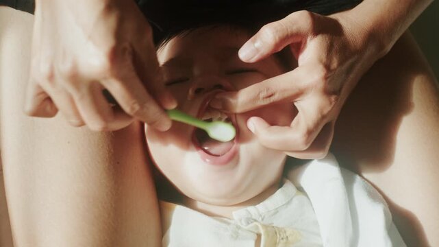 Close up of mother hands cleaning toddler teeth with toothbrush, 4K

