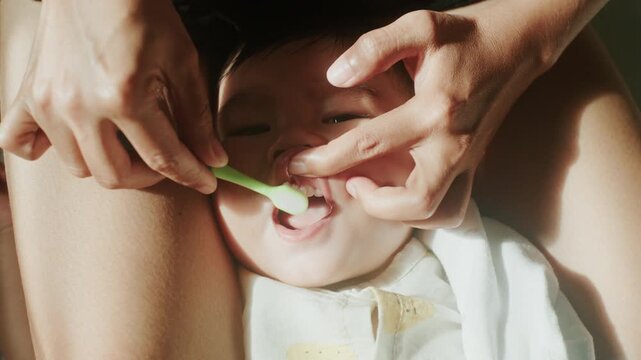Close up of mother hands cleaning toddler teeth with toothbrush, 4K

