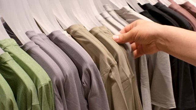 A man's hand selects t-shirt from those hanging on racks in a store.