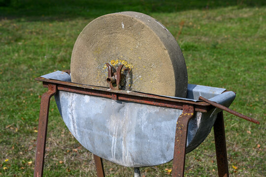 Ancienne meule en pierre avec un bac &agrave; eau sur un support en m&eacute;tal rouill&eacute;. 