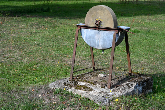 Ancienne meule en pierre avec un bac &agrave; eau sur un support en m&eacute;tal rouill&eacute;. 