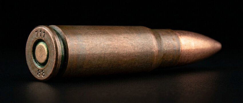 Single metallic bullet for firearms close up studio shot on black background
