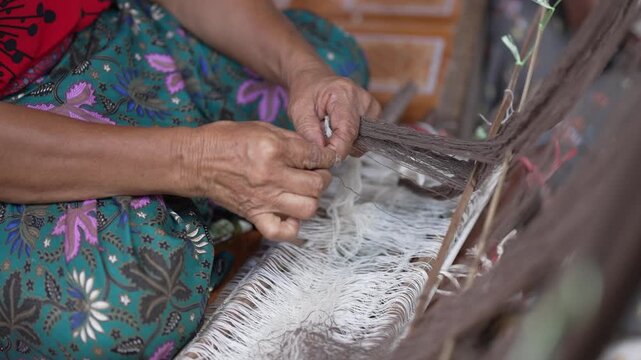Close up of an elderly woman's hands preparing and tying threads on a traditional wooden loom.