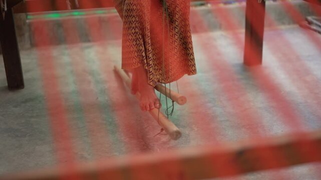 Close up of a weaver's bare feet operating the wooden pedals of a traditional floor handloom.