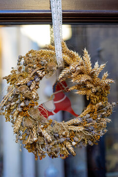 Handmade rustic wreath crafted from dried wheat and wildflowers hanging on a window, natural seasonal decoration with intricate botanical textures.
