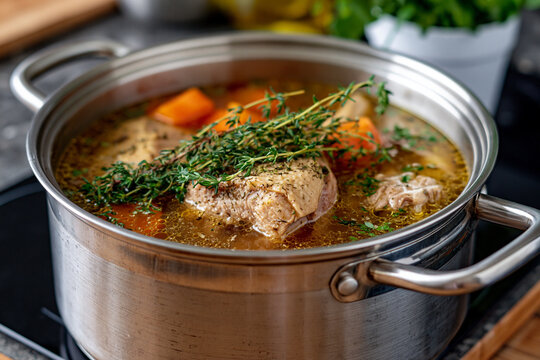 Chicken or turkey soup simmering in a stainless steel pot on a stove, preparing a healthy homemade meal with carrots, broth, and fresh thyme herbs for dinner