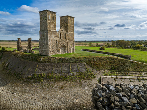 Elevated view of the medieval twin spires of Reculver Towers (The Twin Sisters) and coastal defense wall overlooking green fields in Kent, England
