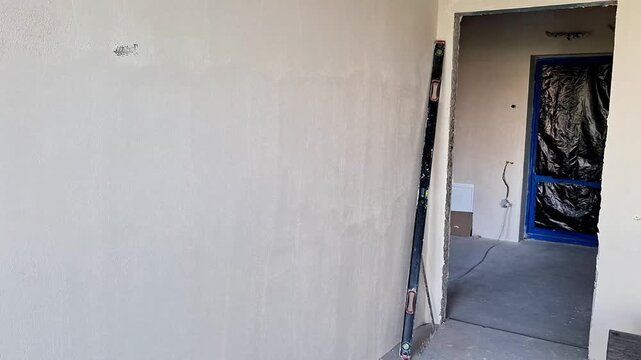 Unfinished interior with a freshly plastered wall, protected doorway, exposed door frame, and construction materials visible during ongoing home renovation work