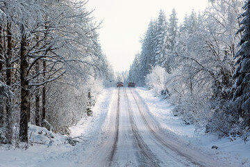 Fototapeta premium Two cars driving along a snow-covered road through a winter forest