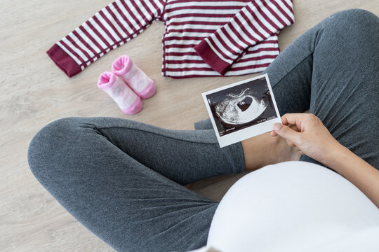 pregnant woman is looking at an ultrasound photo of fetus. Mother gently touches the baby on stomach. Happy, family, growth, pregnancy, enjoyment , prepare newborn, take care, healthcare, tummy.