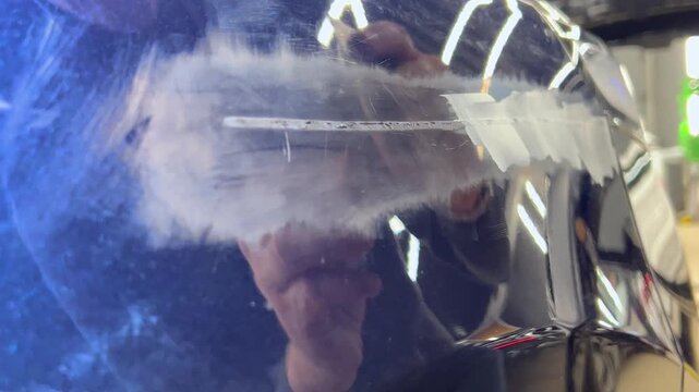Professional auto mechanic man hands applying polyester car body filler putty with a steel spatula knife tool on a damaged blue vehicle part inside a detailing studio. Professional vehicle bodywork. 