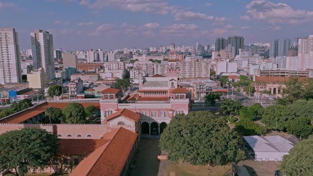 aerial drone orbit around the pink facade of the historic Catavento Cultural Museum amidst the dense urban high-rise skyline of Sao Paulo, Brazil