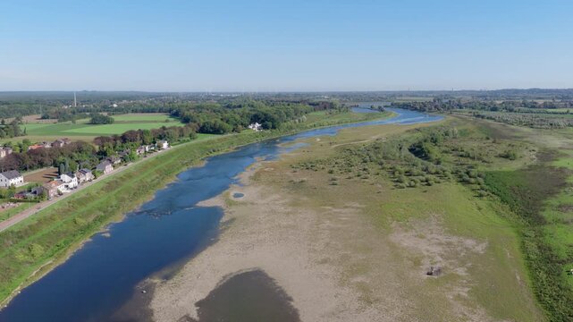 Aerial drone video tilting up to reveal the low water levels and exposed sandbanks of the River Meuse surrounded by green countryside in Lanaken, Belgium. Concept of summer drought and nature.