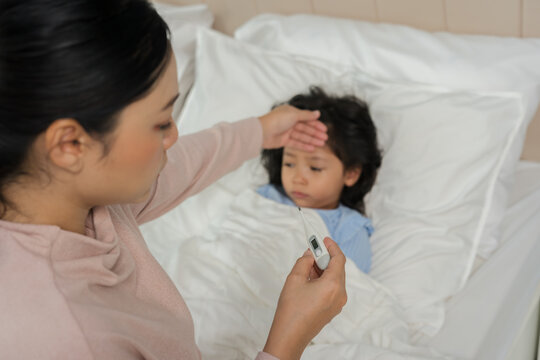 mother using thermometer measuring temperature to checking fever of sick preschoool child girl while hand touching forehead in bed